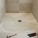 Douche italienne récemment rénovée où de l’eau stagne autour de la bonde, suggérant un problème de pente ou d’évacuation.