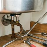 Remplacement d’un robinet de cuisine avec d’anciens flexibles rouillés et de nouveaux tuyaux tressés sous l’évier.
