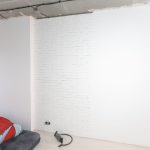 Personne appliquant une couche de peinture sur un mur en placo avec un rouleau.