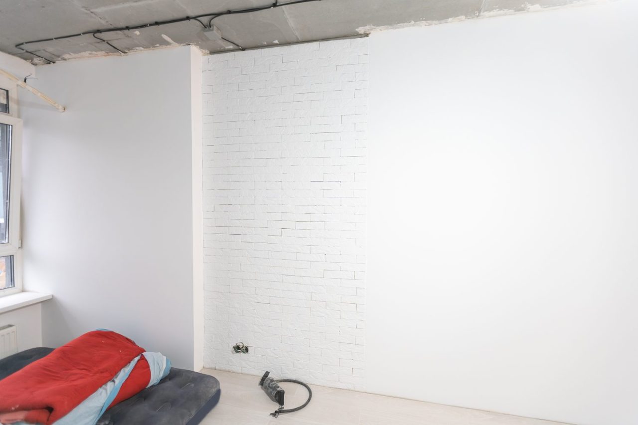 Personne appliquant une couche de peinture sur un mur en placo avec un rouleau.